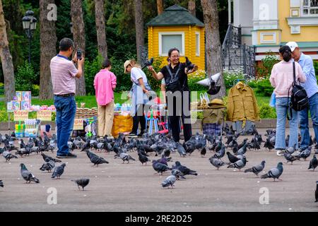 Kazakhstan, Almaty. Femme posant pour photo avec des pigeons, cathédrale de l'Ascension, orthodoxe russe, dans le parc des gardes de Panfilov. Banque D'Images