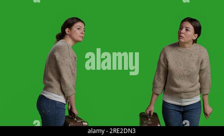 Jeune femme portant une mallette vintage devant la caméra, tenant une valise en studio avant de partir en voyage. Personne joyeuse agissant optimiste et ayant des sacs de voyage ou des bagages sur greenscreen. Banque D'Images