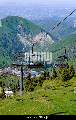 Kazakhstan, Almaty. Descente sur le funiculaire de Shymbulak depuis la zone de ski. Almaty City en arrière-plan lointain. Banque D'Images