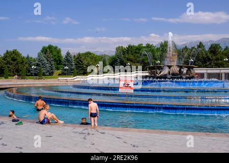 Kazakhstan, Almaty. Garçons jouant dans President's Park Fountain en face de No Swimming Sign. Banque D'Images