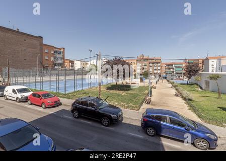 Vue sur un parc avec quelques arbres au feuillage rougeâtre, quelques terrains de sport municipaux et des véhicules stationnés dans la rue Banque D'Images