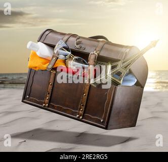 Boîte de vacances, avec des choses du voyage. Des lunettes de soleil, la Tour Eiffel, une bouteille de lotion bronzante dépassent du tronc. Le tronc flotte au-dessus d'une plage Banque D'Images