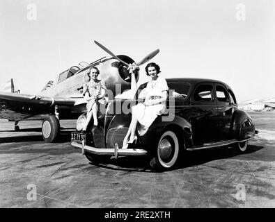 Californie : 1939 deux femmes sont assises sur les ailes d'une berline Lincoln Zephyr de 1939 dans un aéroport avec un avion monomoteur garé derrière elles Banque D'Images