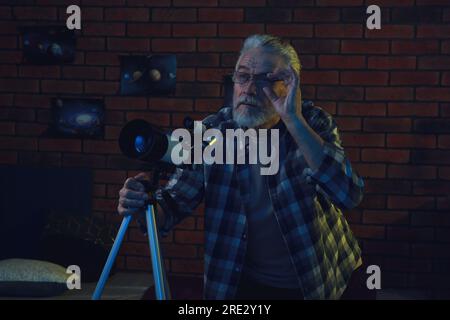Homme âgé utilisant le télescope pour regarder les étoiles dans la chambre Banque D'Images
