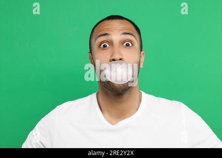 Portrait de jeune homme soufflant de la gomme à bulles sur fond vert Banque D'Images