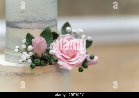 Une image artistique d'un gâteau de mariage blanc à trois niveaux orné de roses et de perles roses Banque D'Images