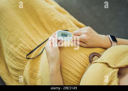 Femme enceinte avec oxymètre de pouls sur le doigt. Médecin mesurant le niveau de saturation en oxygène en visitant la mère expectative avec la maladie de coronavirus à Banque D'Images