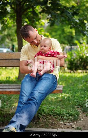 Père assis sur un banc dans le parc et tenant sa petite fille Banque D'Images