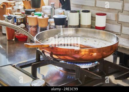 Le lait et les oignons hachés sont frits dans une casserole en cuivre sur un feu à gaz. Banque D'Images