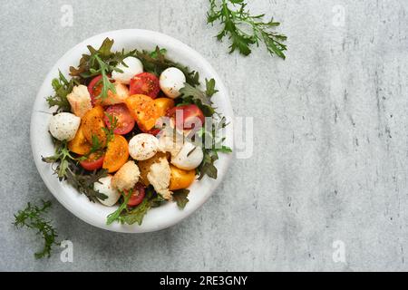 Panzanella toscane. Salade de tomates cerises avec roquette, basilic, mozzarella et craquelins sur un bol blanc. Salade italienne traditionnelle. Méditerranéen HE Banque D'Images