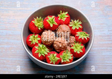 Un bol de grappes rondes de noix de chocolat avec des fraises fraîches entourant les boules de chocolat qui sont placées au centre du bol Banque D'Images