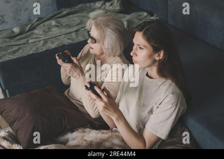 Grand-mère avec sa fille jouant à un jeu vidéo avec des joysticks dans le salon assis sur le sol. Jouer à des jeux vidéo à la maison. Pour la conception de jeux Banque D'Images