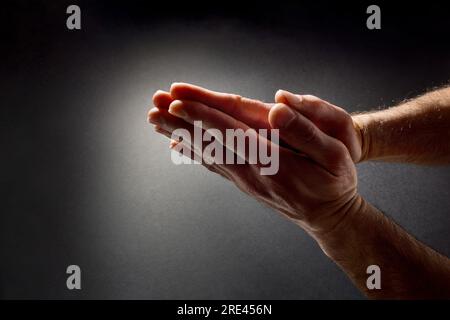 Homme priant avec les mains avec les paumes ensemble contrastés avec le faisceau de lumière sur fond dégradé isolé sombre. Vue de dessus. Banque D'Images