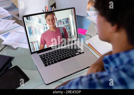 Vue arrière d'un garçon biracial ayant un appel vidéo avec un garçon caucasien sur ordinateur portable à la maison Banque D'Images