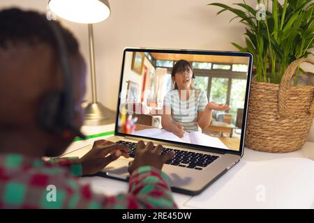 Vue arrière d'un garçon afro-américain utilisant un ordinateur portable tout en ayant un appel vidéo avec une fille asiatique à la maison Banque D'Images