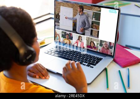 Garçon biracial ayant une vidéoconférence avec professeur masculin caucasien et divers étudiants sur ordinateur portable Banque D'Images