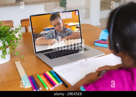 Vue arrière d'une fille biraciale ayant un appel vidéo avec un garçon caucasien sur ordinateur portable à la maison Banque D'Images