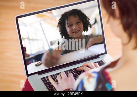 Vue arrière d'une fille caucasienne utilisant un ordinateur portable tout en ayant un appel vidéo avec un garçon biracial à l'école Banque D'Images