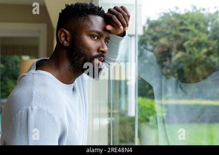 Homme afro-américain réfléchi regardant par la fenêtre à la maison Banque D'Images
