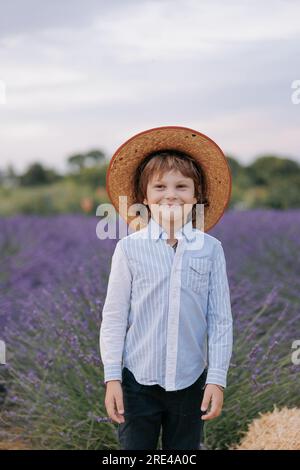 Joyeux enfant garçon dans le chapeau debout sur fond de champ de lavande en fleurs et de ciel. Banque D'Images