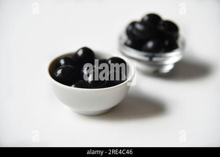 Olives noires dans une casserole blanche et en verre sur fond blanc. Nourriture végétarienne. Banque D'Images