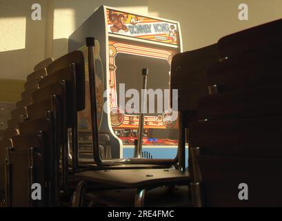 Une armoire de jeux vidéo d'arcade Nintendo Donkey Kong sur un mur jaune dans une pièce flanquée de chaises empilées éclairées par une lumière de fenêtre - 25 juillet 2023 Banque D'Images