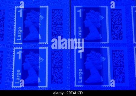 Angleterre, 25 juillet 2023 : comparaison : gauche, timbres contrefaits, droite, timbres authentiques sous lumière UV. Les timbres authentiques ont une ombre supplémentaire au-delà du nez de la reine Elizabeth II. Le papier dorsal est également moins réactif à la lumière UV. Les perforations ovales de sécurité le long des deux côtés réagissent avec la lumière UV sur les faux par rapport aux timbres authentiques sur la droite. - Contrefaçons Royal Mail timbres à code-barres sont en vente sur eBay à une fraction du prix réel. Des feuilles de 50 timbres sont en vente aussi bas que 15 livres (GBP) et à l'oeil peu méfiant ont l'air réel. Crédit : Arrêter Press Media/Alamy Live News Banque D'Images