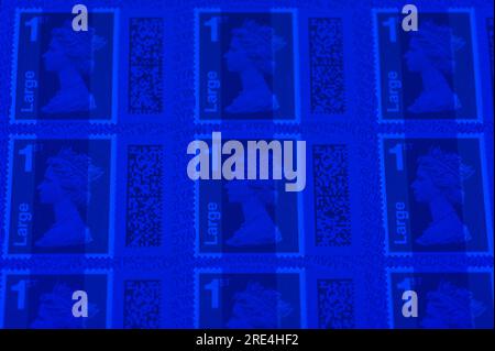 Angleterre, le 25 juillet 2023 : faux timbres Royal Mail 1st Class large Letter sous lumière UV. - Contrefaçons Royal Mail timbres à code-barres sont en vente sur eBay à une fraction du prix réel. Des feuilles de 50 timbres sont en vente aussi bas que 15 livres (GBP) et à l'oeil peu méfiant ont l'air réel. Cependant, sous la lumière UV, de petites différences peuvent être observées. Crédit : Arrêter Press Media/Alamy Live News Banque D'Images