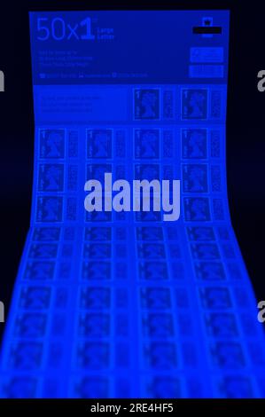 Angleterre, le 25 juillet 2023 : faux timbres Royal Mail 1st Class large Letter sous lumière UV. - Contrefaçons Royal Mail timbres à code-barres sont en vente sur eBay à une fraction du prix réel. Des feuilles de 50 timbres sont en vente aussi bas que 15 livres (GBP) et à l'oeil peu méfiant ont l'air réel. Cependant, sous la lumière UV, de petites différences peuvent être observées. Crédit : Arrêter Press Media/Alamy Live News Banque D'Images