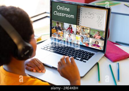 Vue arrière d'un garçon biracial ayant une vidéoconférence avec divers étudiants sur ordinateur portable à la maison Banque D'Images