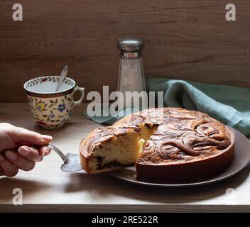 Gâteau au chocolat maison fraîchement cuit - brownie dans une forme ronde, à la main en sortant un morceau. Vue avant. Banque D'Images