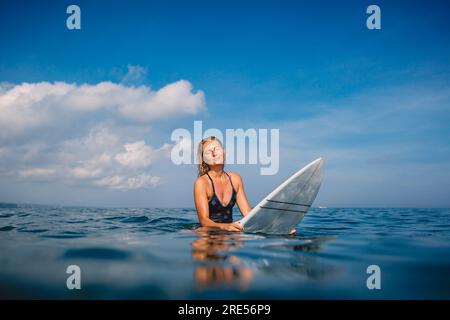 Surfeuse femme assise sur la planche de surf et attendant les vagues. Femme avec planche de surf dans l'océan Banque D'Images