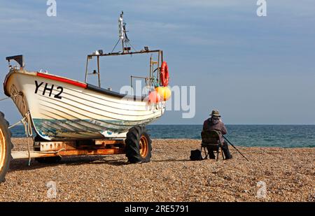 Un ornithologue assis sous le vent d'un bateau de pêche côtière observant les oiseaux au-dessus de la mer à Cley Next the Sea, Norfolk, Angleterre, Royaume-Uni. Banque D'Images