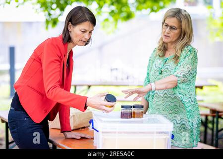Hanovre, Allemagne. 25 juillet 2023. Miriam Staudte (Bündnis 90/Die Grünen, l), ministre de l'alimentation, de l'Agriculture et de la protection des consommateurs de Basse-Saxe, et Wiebke Langefeld, apiculteur, regardent des pots de miel dans le jardin du ministère de l'Agriculture de Basse-Saxe. Le ministère obtient une troisième colonie d'abeilles. Crédit : Moritz Frankenberg/dpa/Alamy Live News Banque D'Images