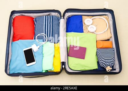 Voir le formulaire ci-dessus d'une valise ouverte emballée avec des vêtements, des accessoires et un passeport sur un lit. Concept de voyage. Banque D'Images