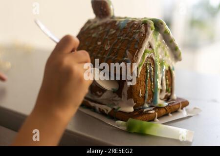 maison en pain d'épice. Petite fille dans les préparations de vacances mettant le vitrage sur la maison de pain d'épice arbres de Noël. Banque D'Images