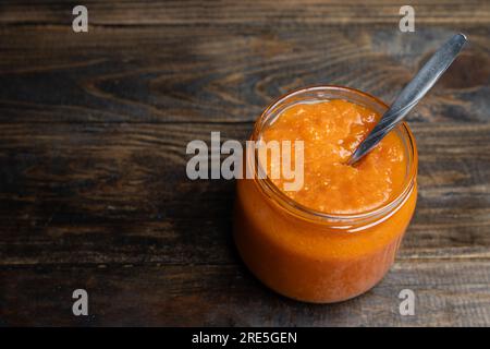 Confiture d'abricot dans un bocal en verre avec une cuillère à l'intérieur sur un fond en bois Banque D'Images