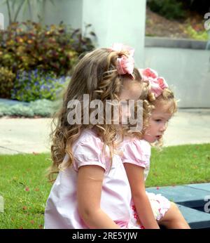 Deux jeunes filles s'assoient côte à côte sur l'herbe dans un parc. Ils regardent tous les deux vers le bas et rêvent de jour. Banque D'Images