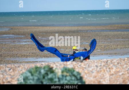 Kitesurfer ou kite surfer luttant dans le vent sur une plage portant un grand cerf-volant pour le kitesurf sur une journée d'été venteuse au bord de la mer en Angleterre, au Royaume-Uni. Banque D'Images