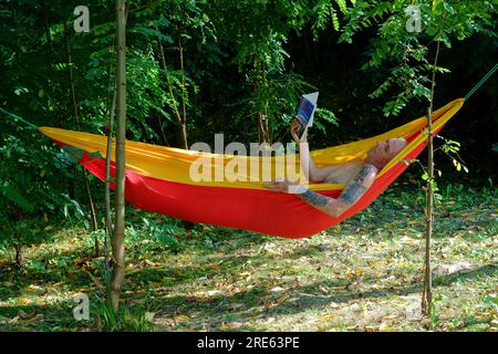 homme plus âgé se relaxant dans le jardin hamac ombragé par les arbres lisant le livre zala comté hongrie Banque D'Images