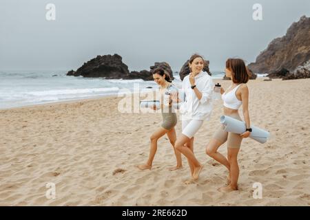 Yoga de plage. Heureux jeunes femmes de fitness se préparant pour des exercices sur la rive de l'océan, profitant de l'entraînement frais à l'extérieur Banque D'Images