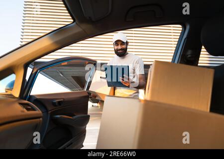 Livreur regardant les boîtes dans la voiture écrire dans le presse-papiers Banque D'Images