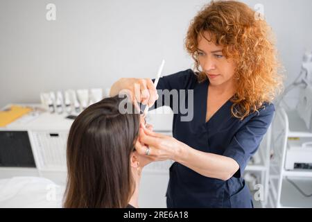 Master applique des marques blanches à la forme correcte du sourcil avec une brosse spéciale. Esthéticienne fait des marques avec un crayon pour le tatouage permanent. Maquillage professionnel et cosmétologie de soins de la peau Banque D'Images