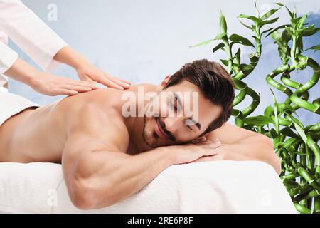 Beau jeune homme recevant un massage du dos dans le salon de spa. Tiges de bambou vert sur fond Banque D'Images