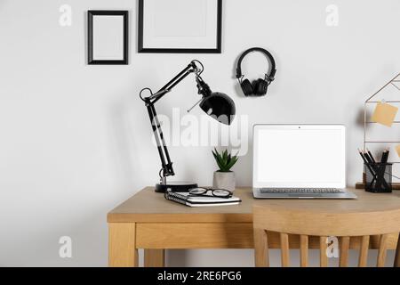 Lieu de travail à domicile. Ordinateur portable, lampe et papeterie sur bureau en bois Banque D'Images