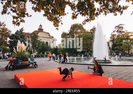 Un enfant joue sur une plate-forme rouge à côté d'une fontaine dans la rue principale de Plovdiv, en Bulgarie Banque D'Images