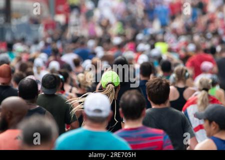 Un chapeau de néon vert solitaire se démarque dans une foule massive de coureurs qui terminent la Peachtree Road Race à Atlanta. Banque D'Images