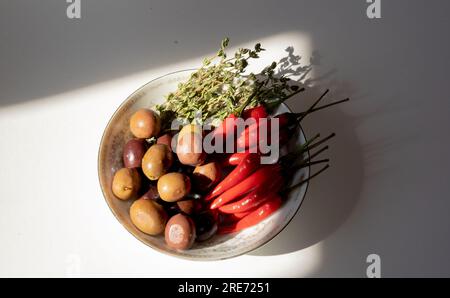 Olives, piments Chili et thym dans une petite assiette ronde Banque D'Images