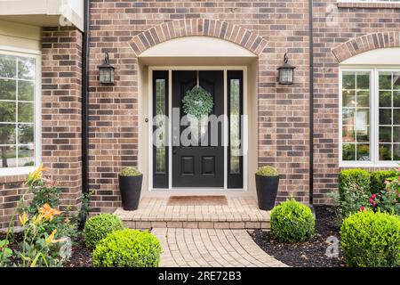 La porte d'entrée d'une maison en brique avec une porte d'entrée noire et un trottoir de chemin de pierre. Banque D'Images