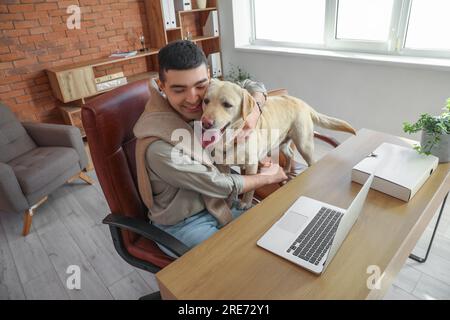 Jeune homme serrant chien Labrador mignon à la table dans le bureau Banque D'Images